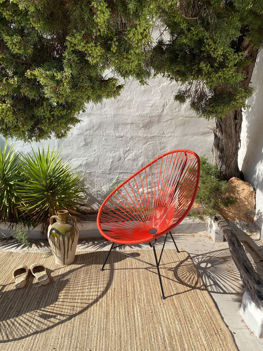 Original-Acapulco-Chair-koralle Original Acapulco Chair in der Farbe koralle vor Wand und Bäumen